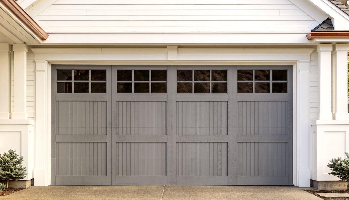 Ett vitt hus med grå garagedörr i trä. Garagedörren har små, spröjsade fönster upptill.