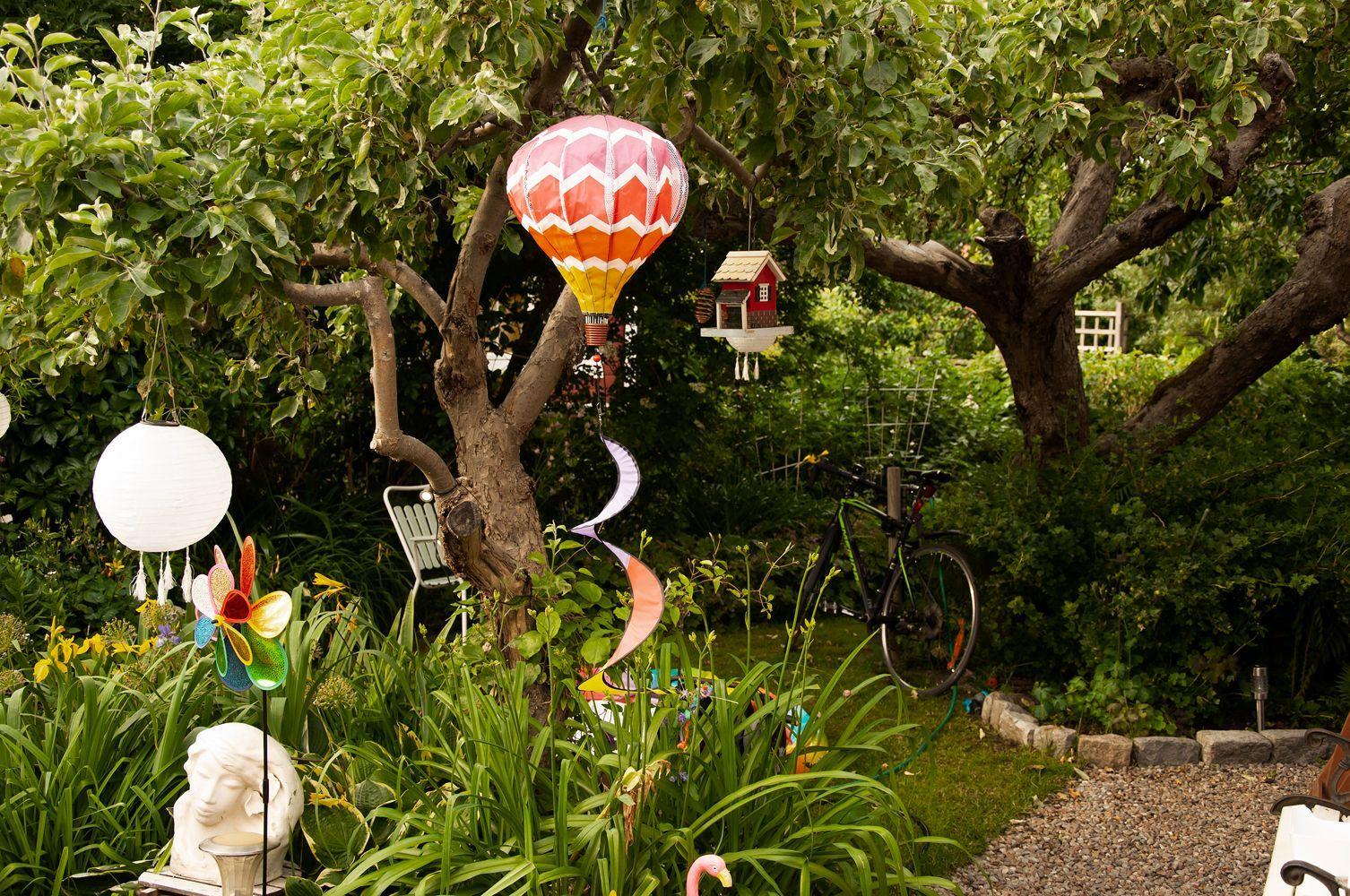 En mysig trädgårdsdunge med färgglada utsmyckningar i form av fågelmatare, luftballong, rislampa, vindsnurror.