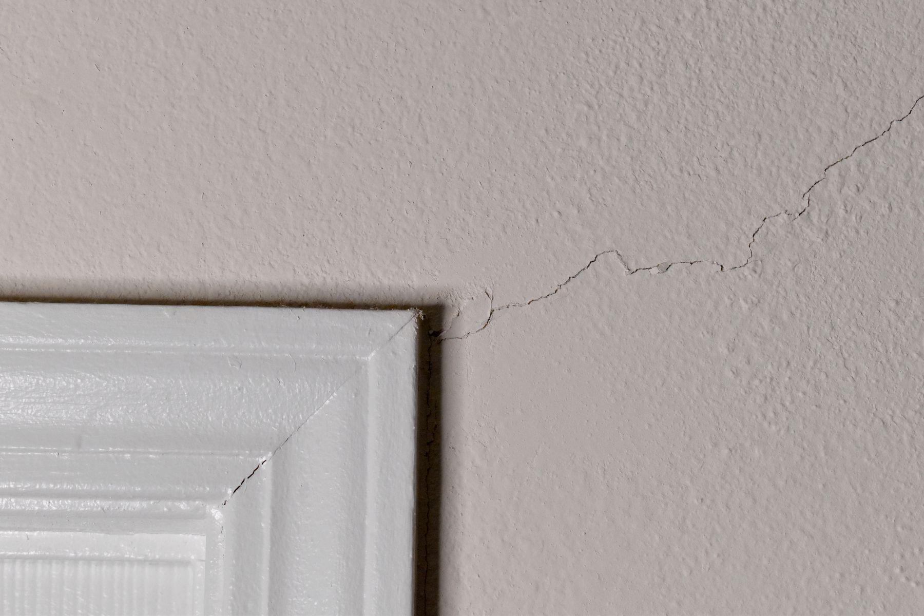 En spricka i väggen från kanten på den vita dörrkarmen och utåt över beige vägg.