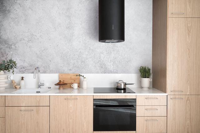 Ett modernt, ljust kök med träluckor och betongliknande vägg. På den vita bänkskivan står diverse kökstillbehör.