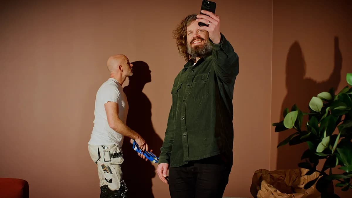 Nöjd kund tar selfie medan professionell målare målar vardagsrum i rostfärgade väggar