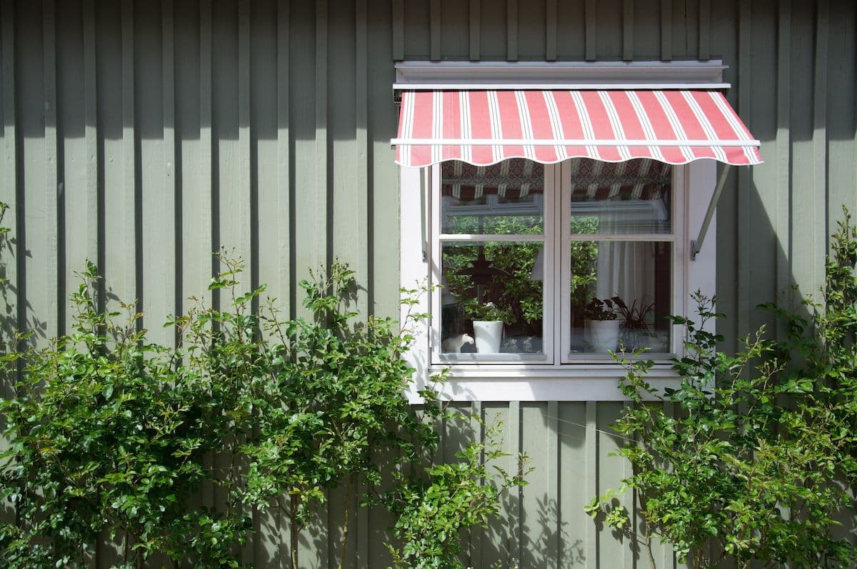 ett fint grönt hus med en röd markis och vitt fönster. Runt om är det gröna buskar.