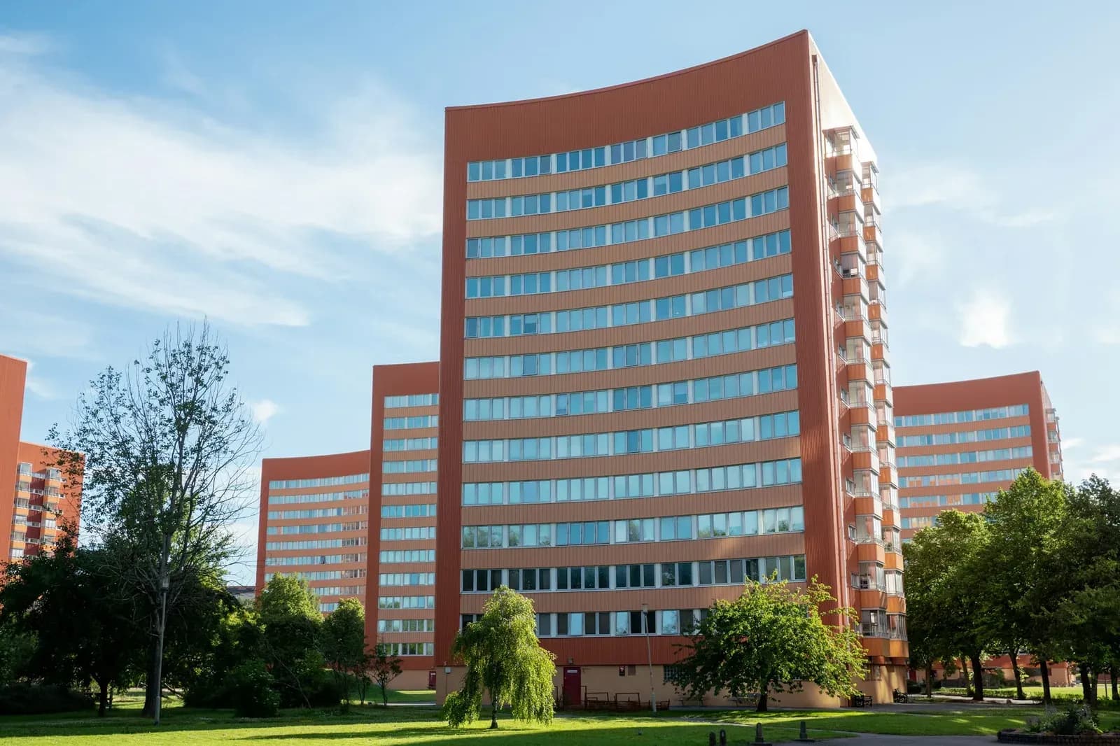Flerbostadshus i rött tegel med grön innergård en solig dag · Foto: Carl Malmer / Unsplash