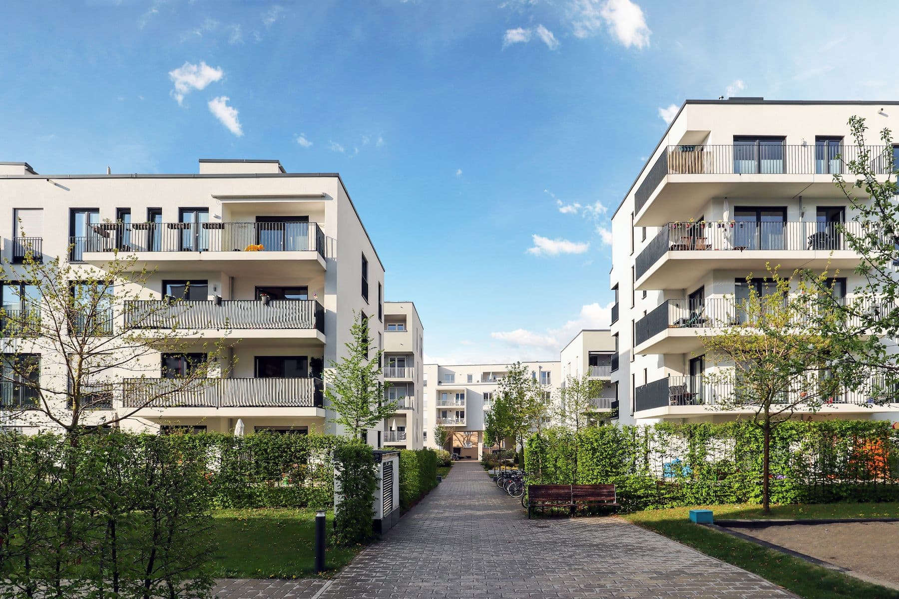 Flerbostaddshus med balkonger, i mellan en stenbelagd gata och gröna buskar på sidorna