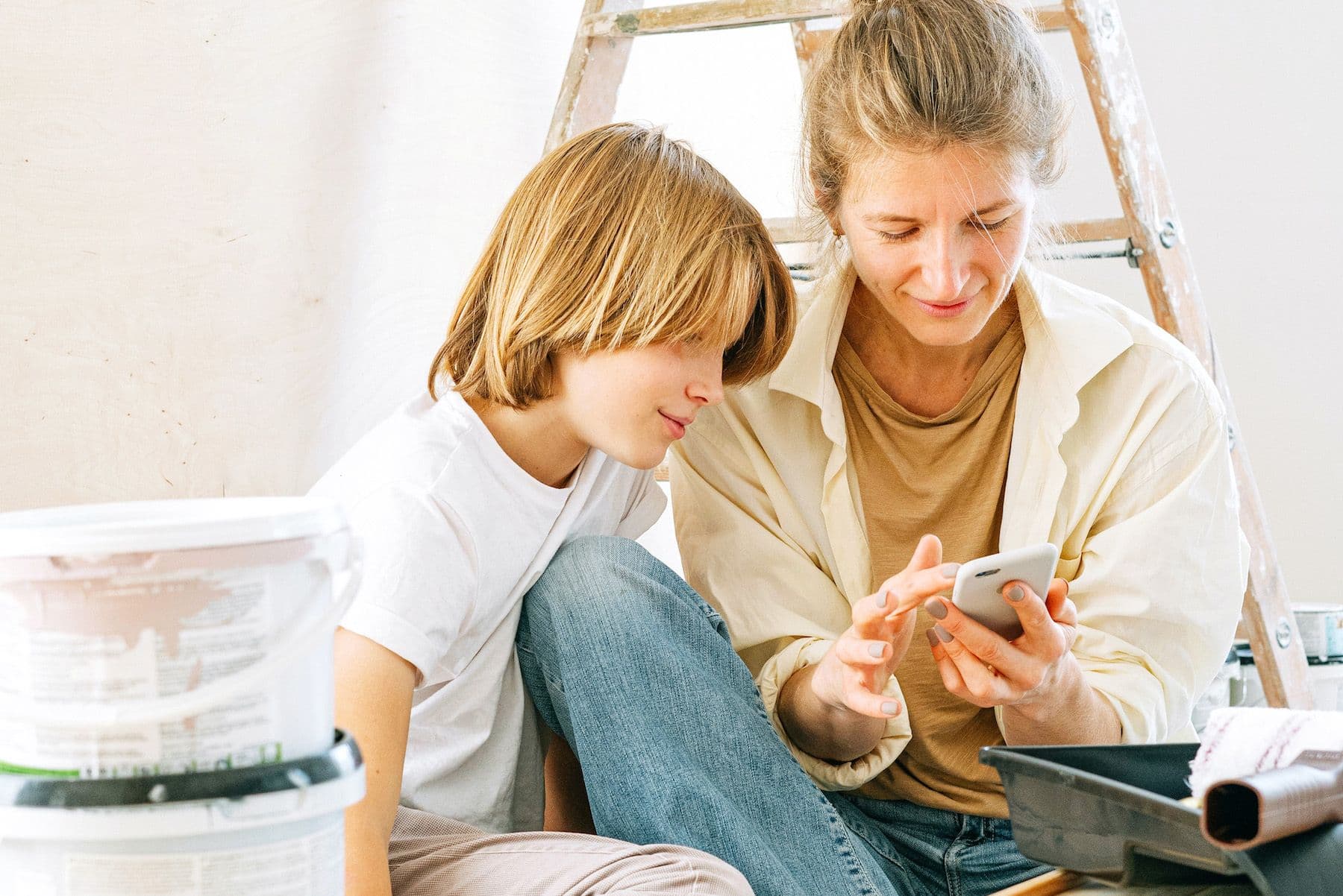 Mamma och barn kontrollerar företag innan de startar renoveringen.  Sitter bland färgburkar och en stege.