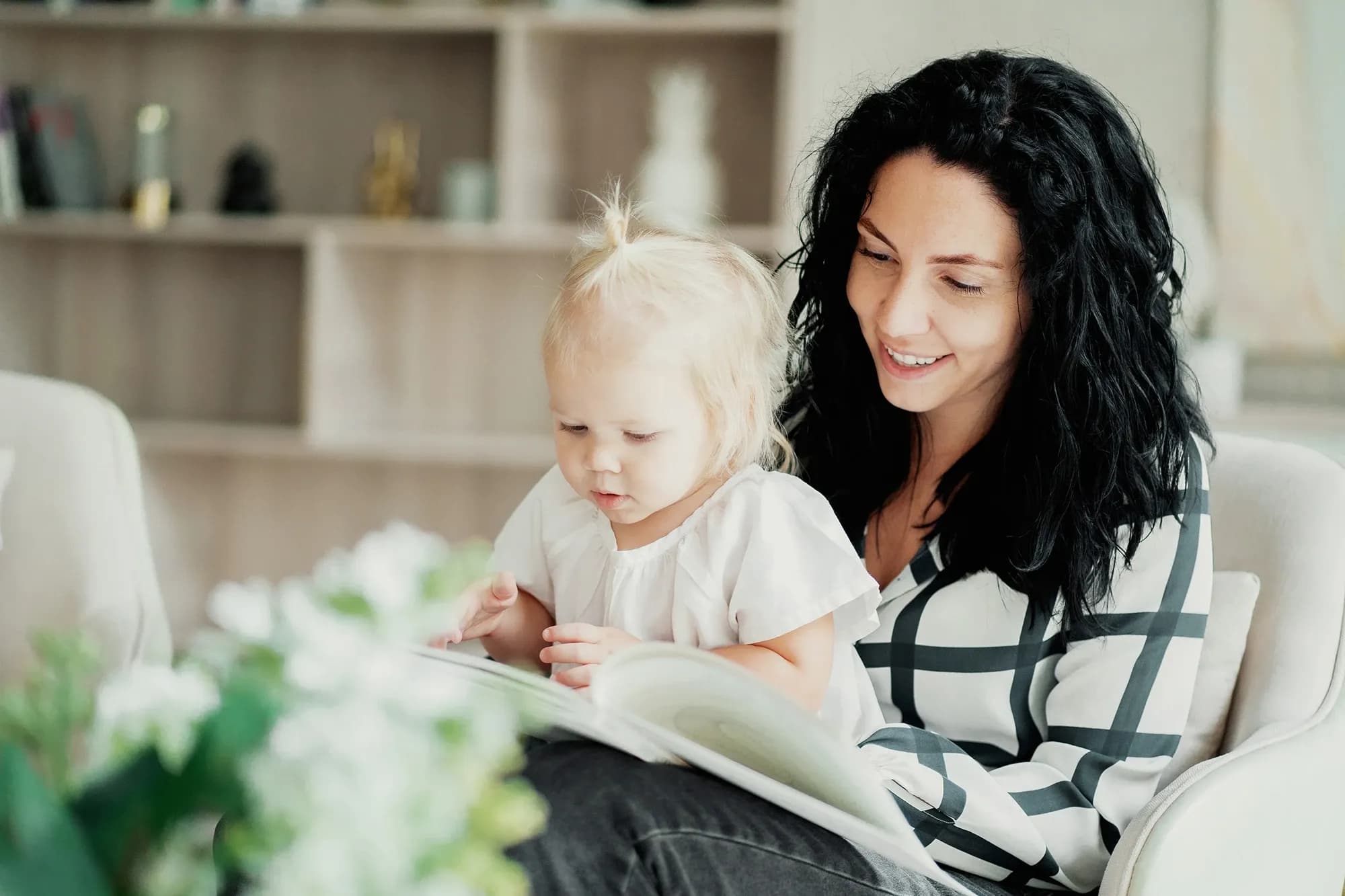 Nanny håller ett barn i knät och läser en bok tillsammans - symboliserar barnpassningstjänst med fokus på omsorgsfull och engagerad barnomsorg