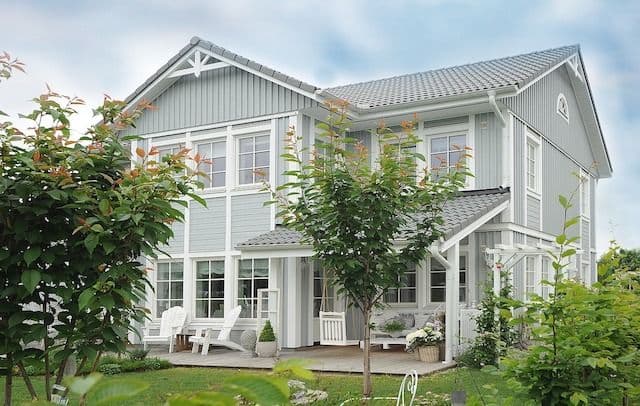 ett stort grått hus med vita lister och fönster. Utanför är en grön trädgård med små träd.