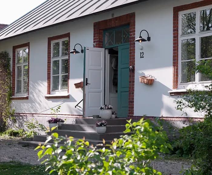 Dörr står på glänt till hus med putsfasad en sommardag