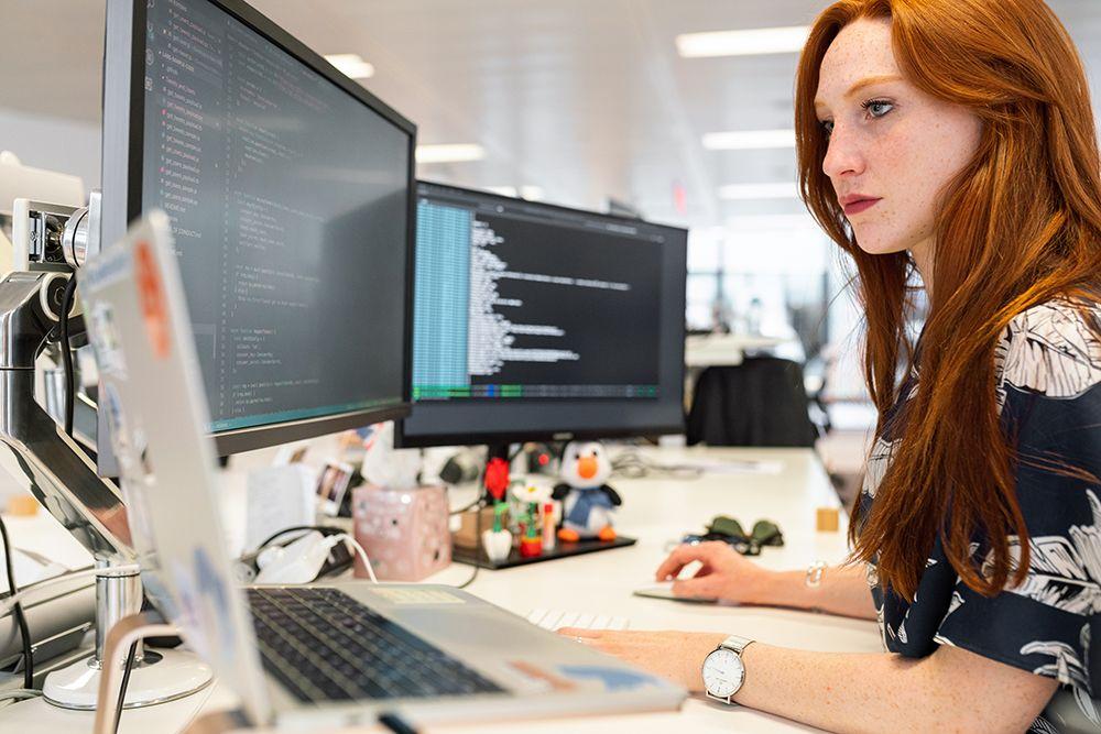 Kvinna med rött hår sitter vid skrivbord och skriver htmlkod