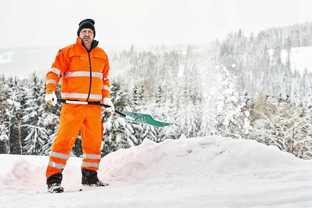 Servicearbetare i uniform med spade röjer snö på vintern