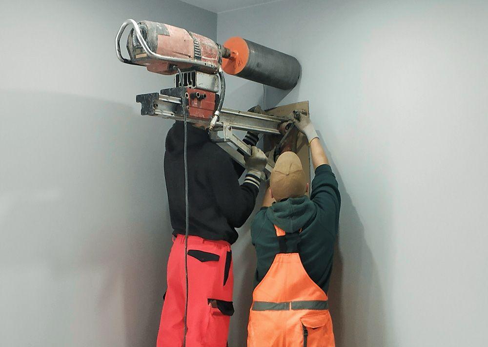 Två arbetare borrar ett hål i en betongvägg med diamantborr