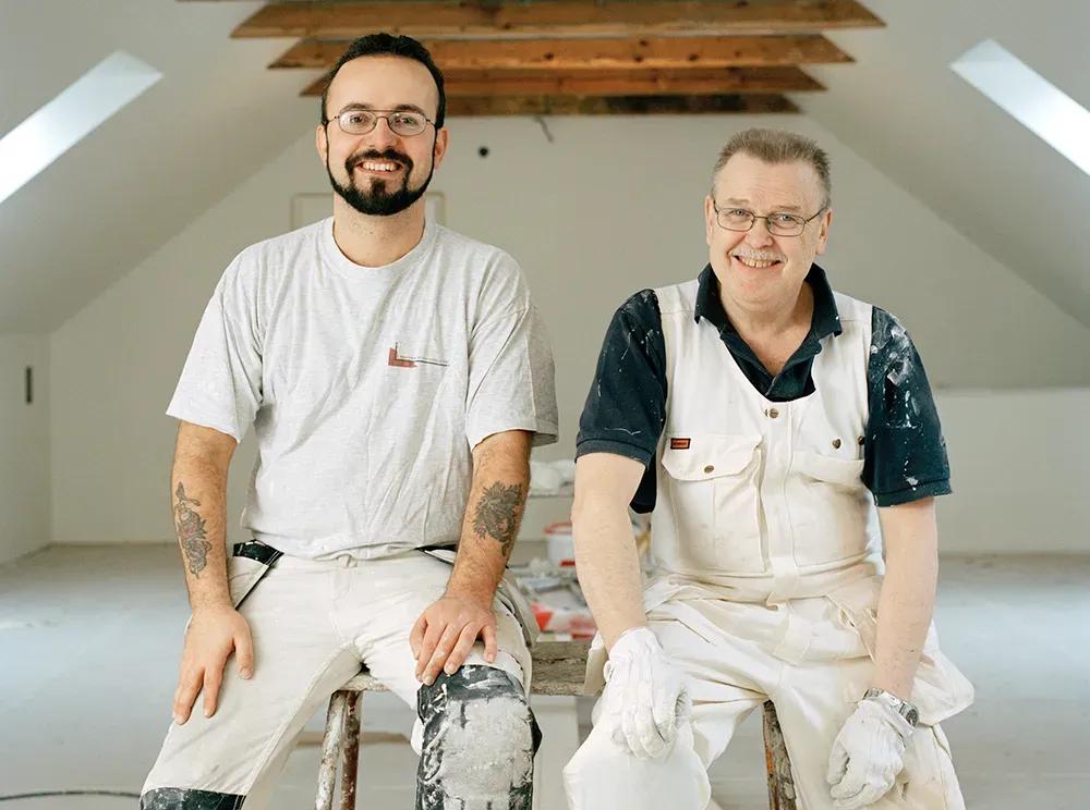 En målare och en hantverkare sitter på en byggpall i ett rum de håller på att renovera