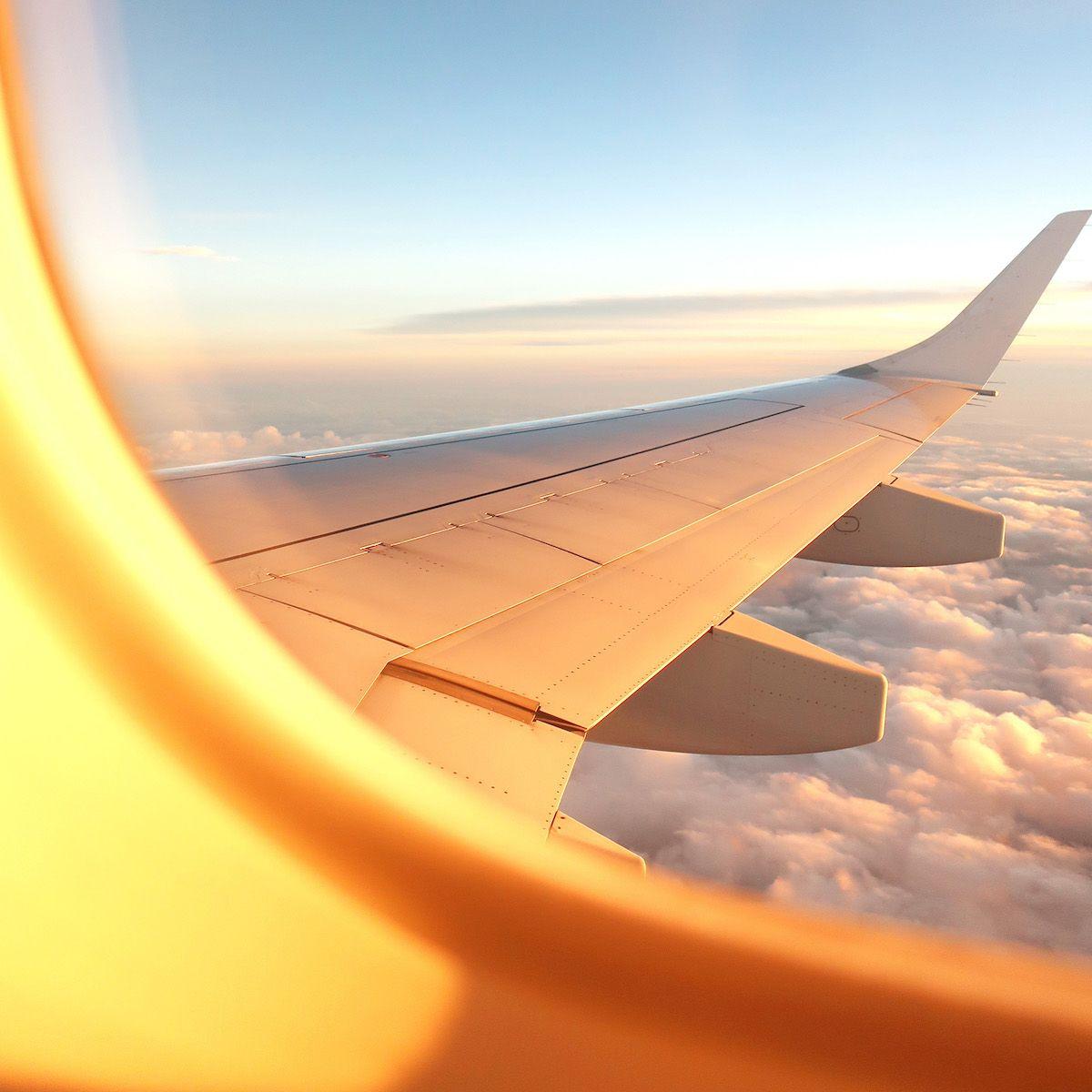 En flygplansvinge i solnedgång tagen från luften. I bilden syns en del av passagerarfönstret på flygplanet.
