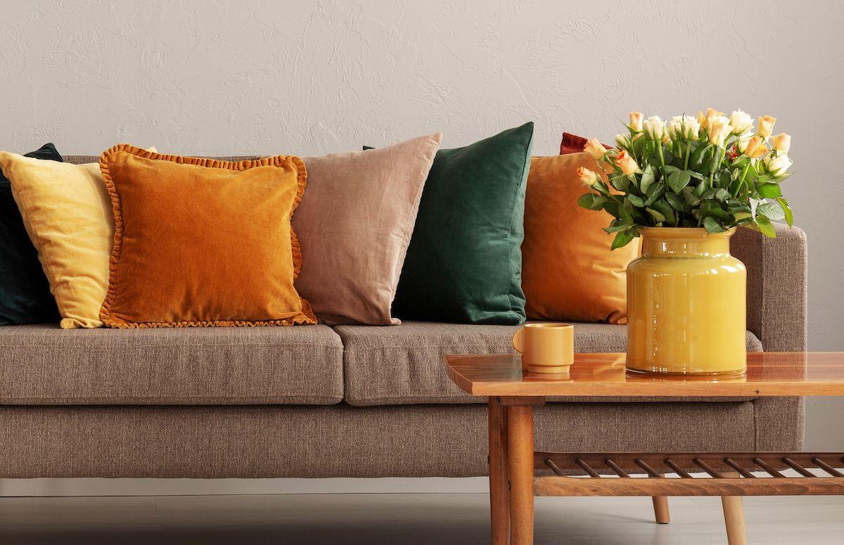 En soffa med färgade kuddar i höstens alla färger, bland annat senapsgul, orange, grön. Framför soffan står ett bord med en vacker blombukett.