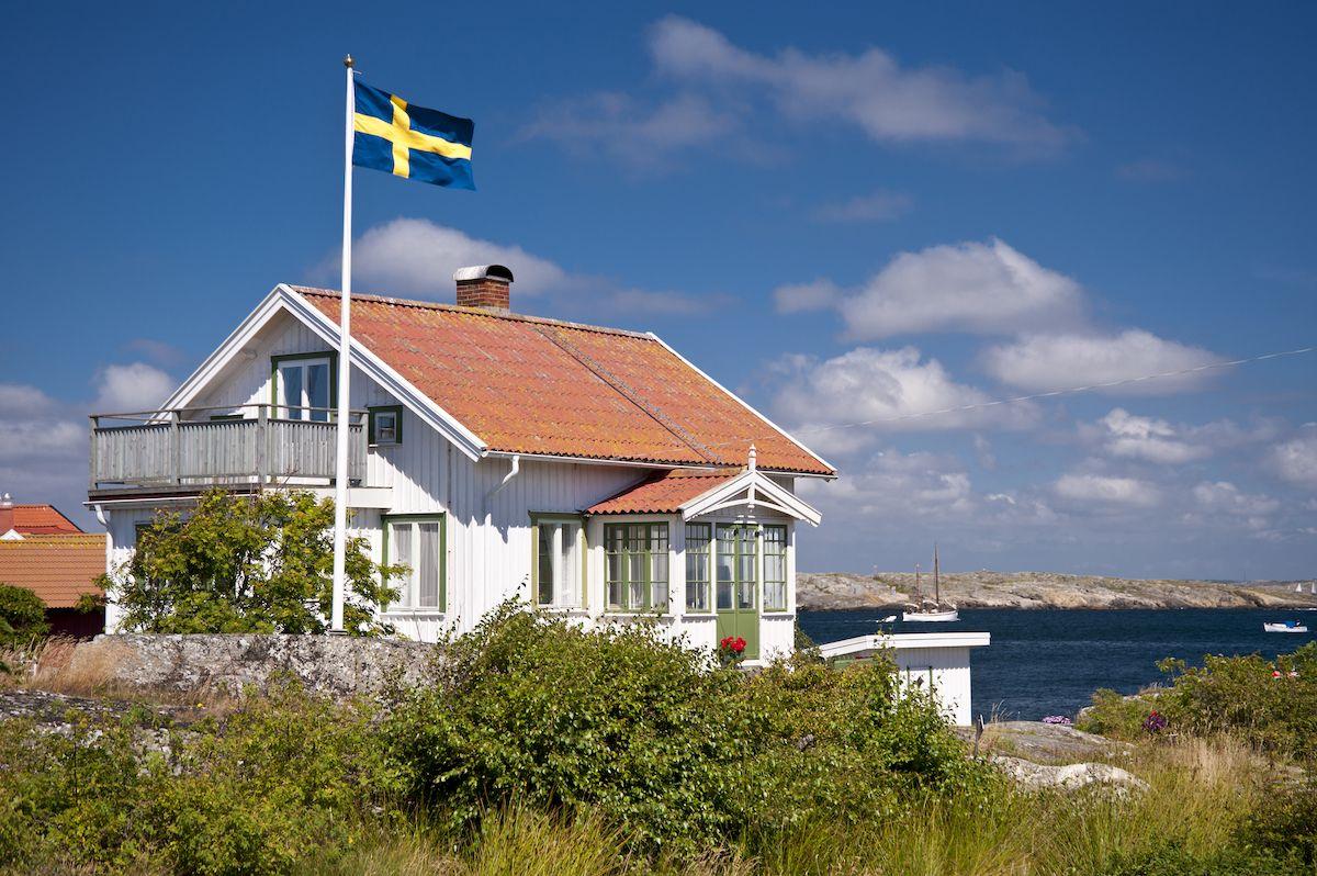 Ett vitt vackert hus vid vattnet en fin sommardag i Sverige. Husets tak är behov av en taktvätt.