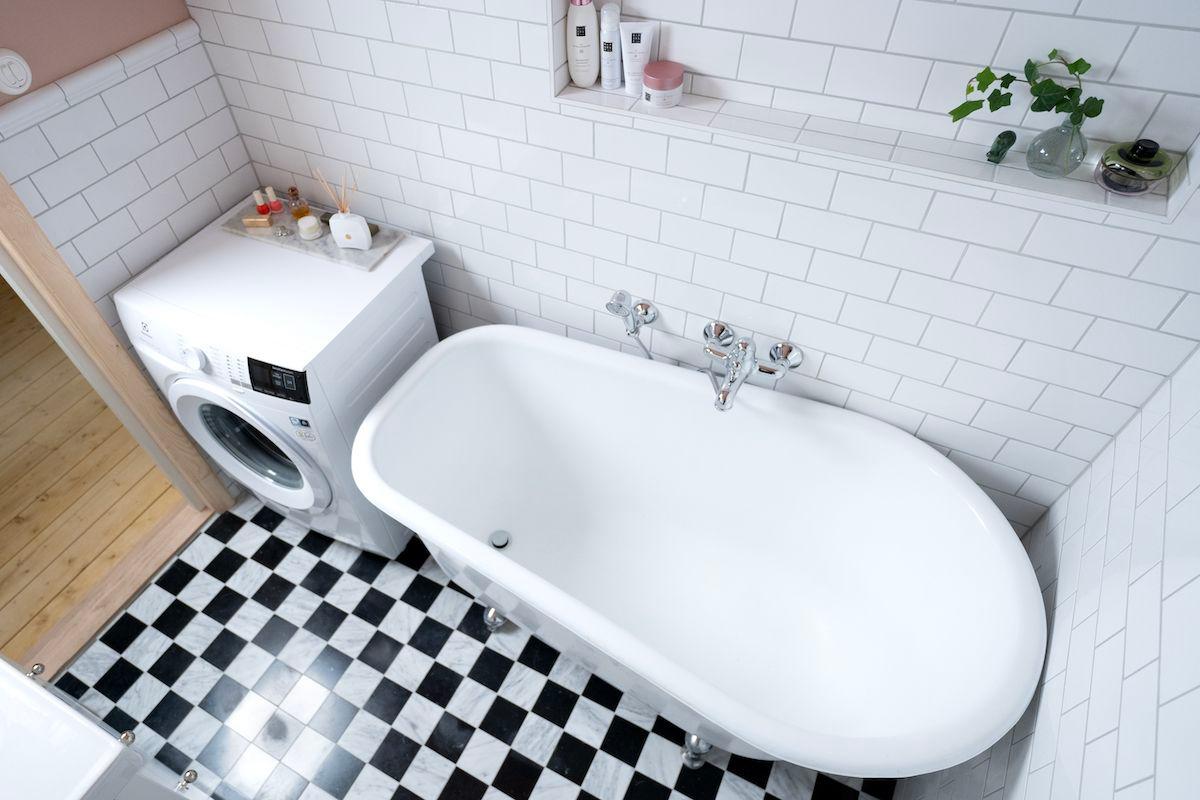 Bild från en badrumsrenovering. På bilden syns det färdiga resultatet med ett vitt badkar, vitt kakel och svartvitt marmorgolv i ett schackrutigt mönster..