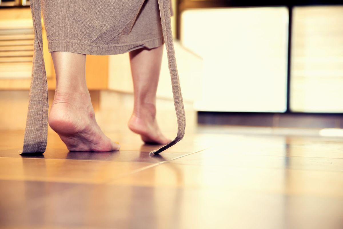 Närbild på ett par fötter som går barfota över ett brun-grått kakelgolv med golvvärme.