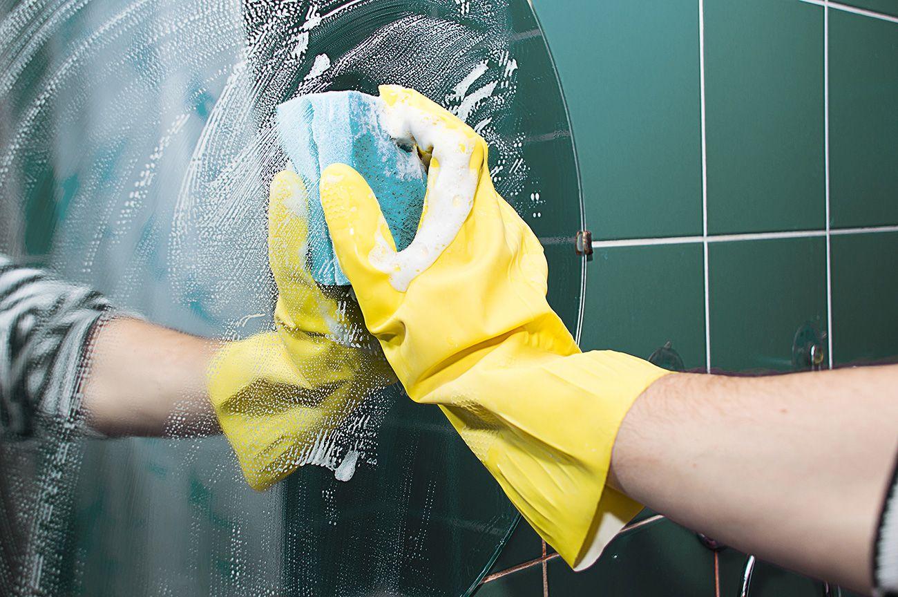 Städare med gula städhandskar tvättar spegel i badrum