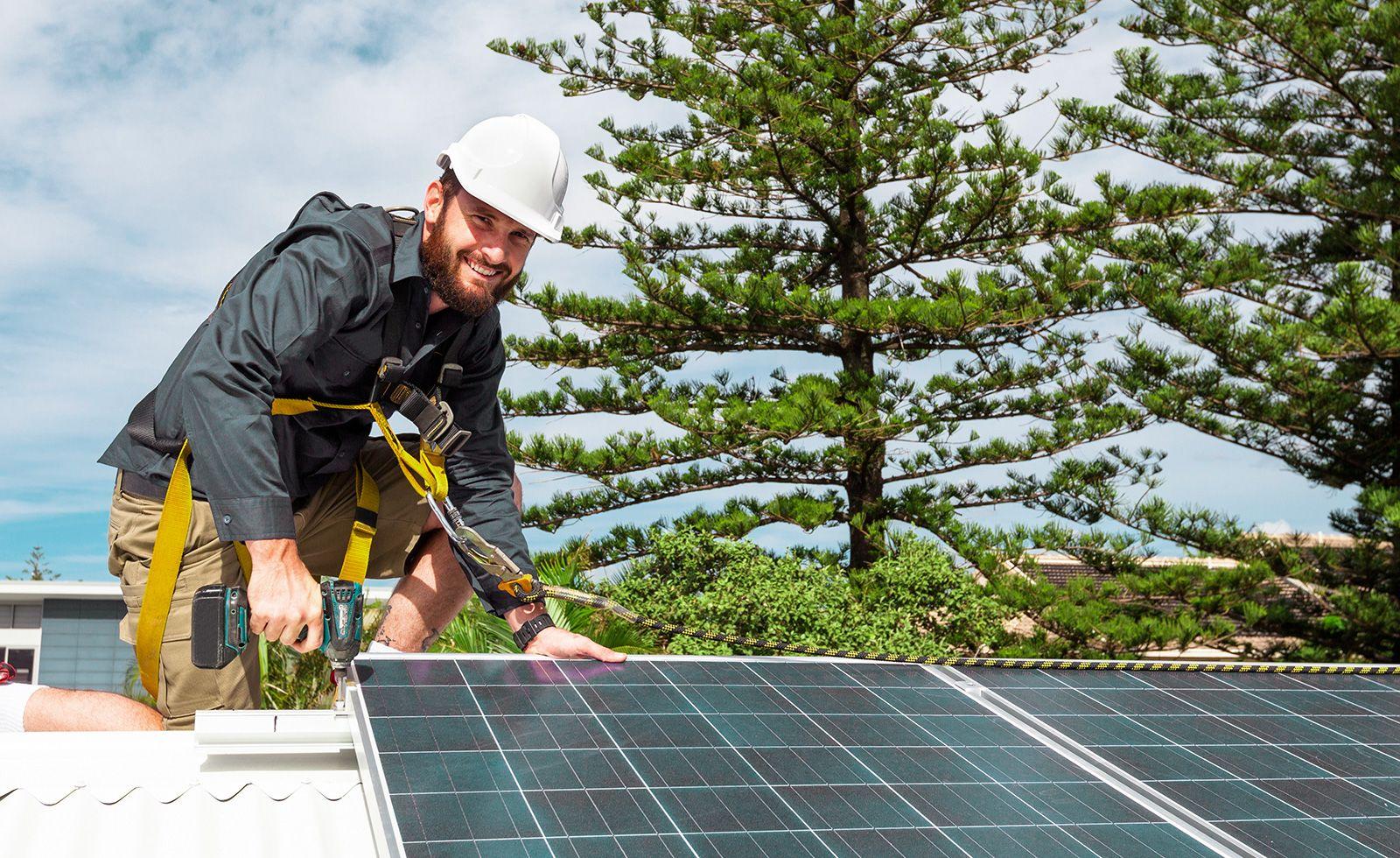 Solcellsinstallatör med skyddssele och hjälm installerar solceller på hustak