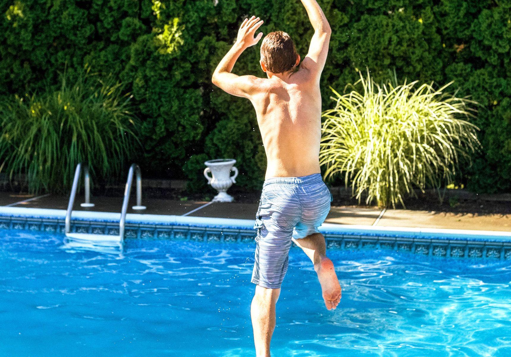 Pojke i ljusblå badbyxor som hoppar i pool