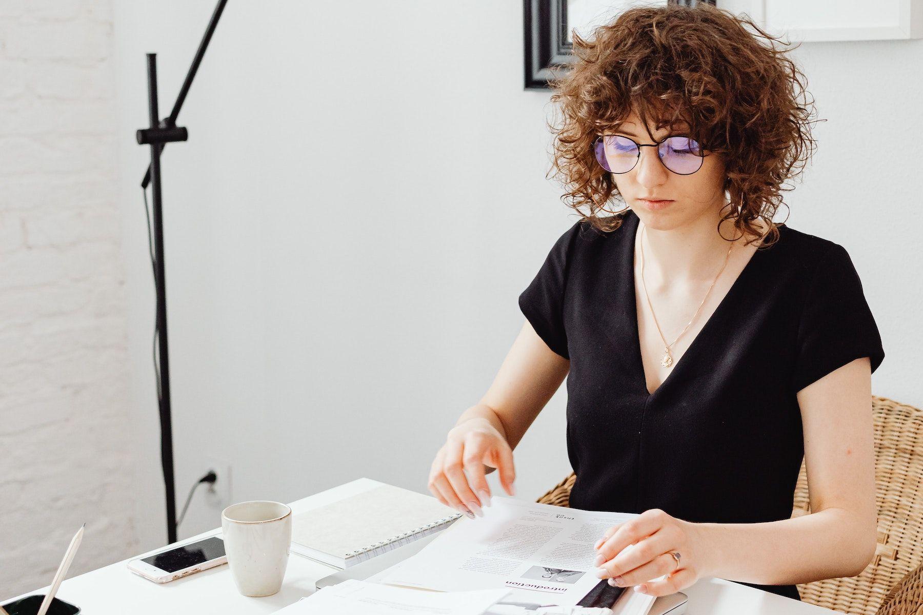 Kvinna som arbetar med papper, har glasögon och lockigt hår