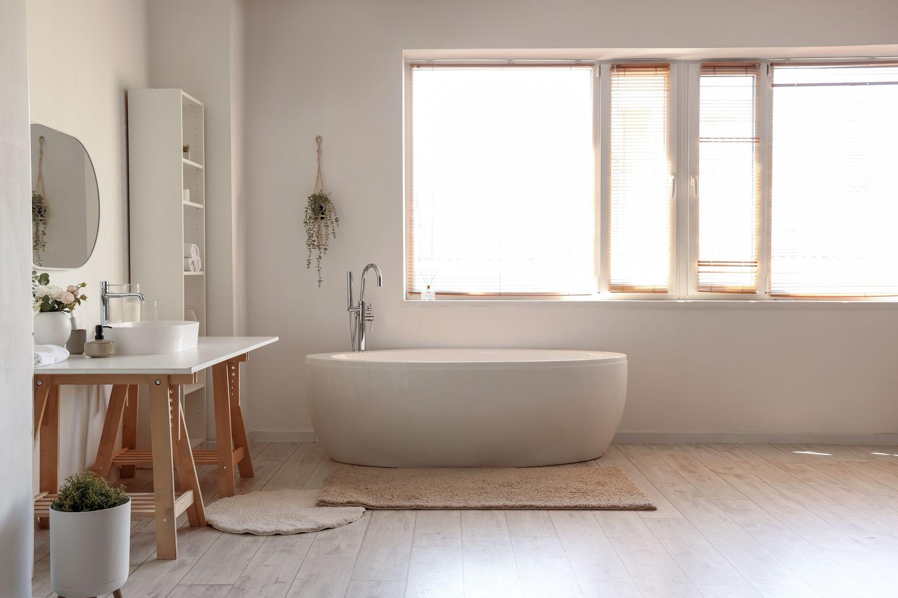 Ljust badrum med väggar i microcement och badkar. Harmonisk inredning med ljusinsläpp från stora fönster.