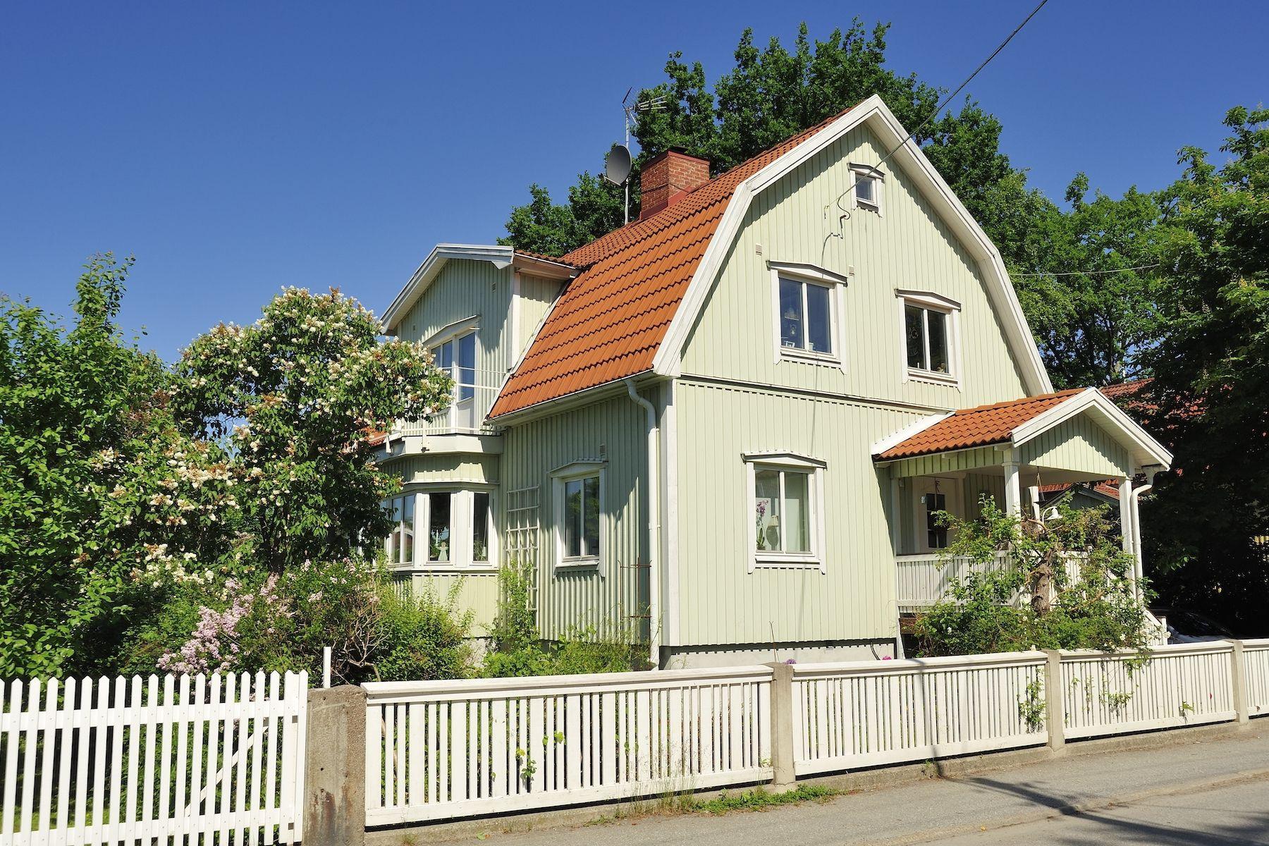 Hus med ljusgrön fasad och tegeltak, vitt staket