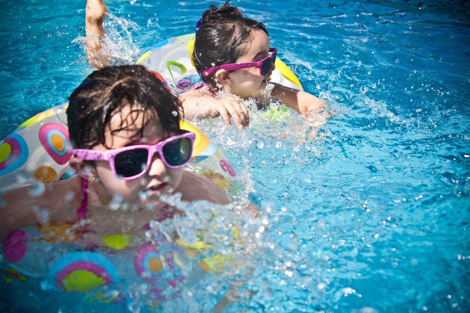 Två barn med rosa glasögon och färgglada badringar badar i en pool