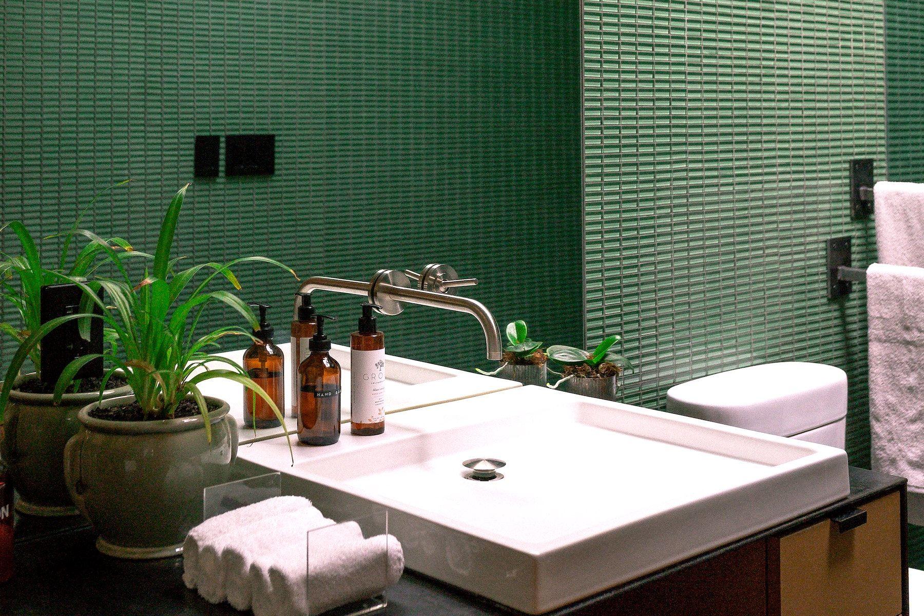 Badrum med grönt kakel och ett handfat med dekorerande växter på sidan
