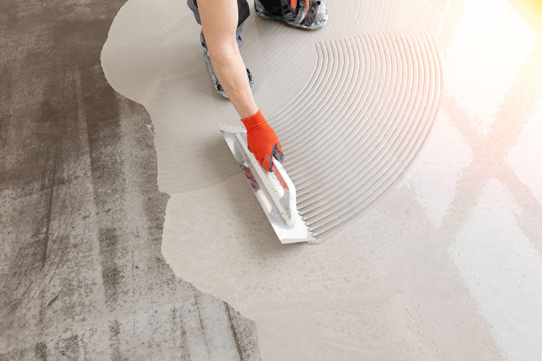 Microcement i ljusgrå/beige färgton appliceras på golv med en spackelliknande skrapa.