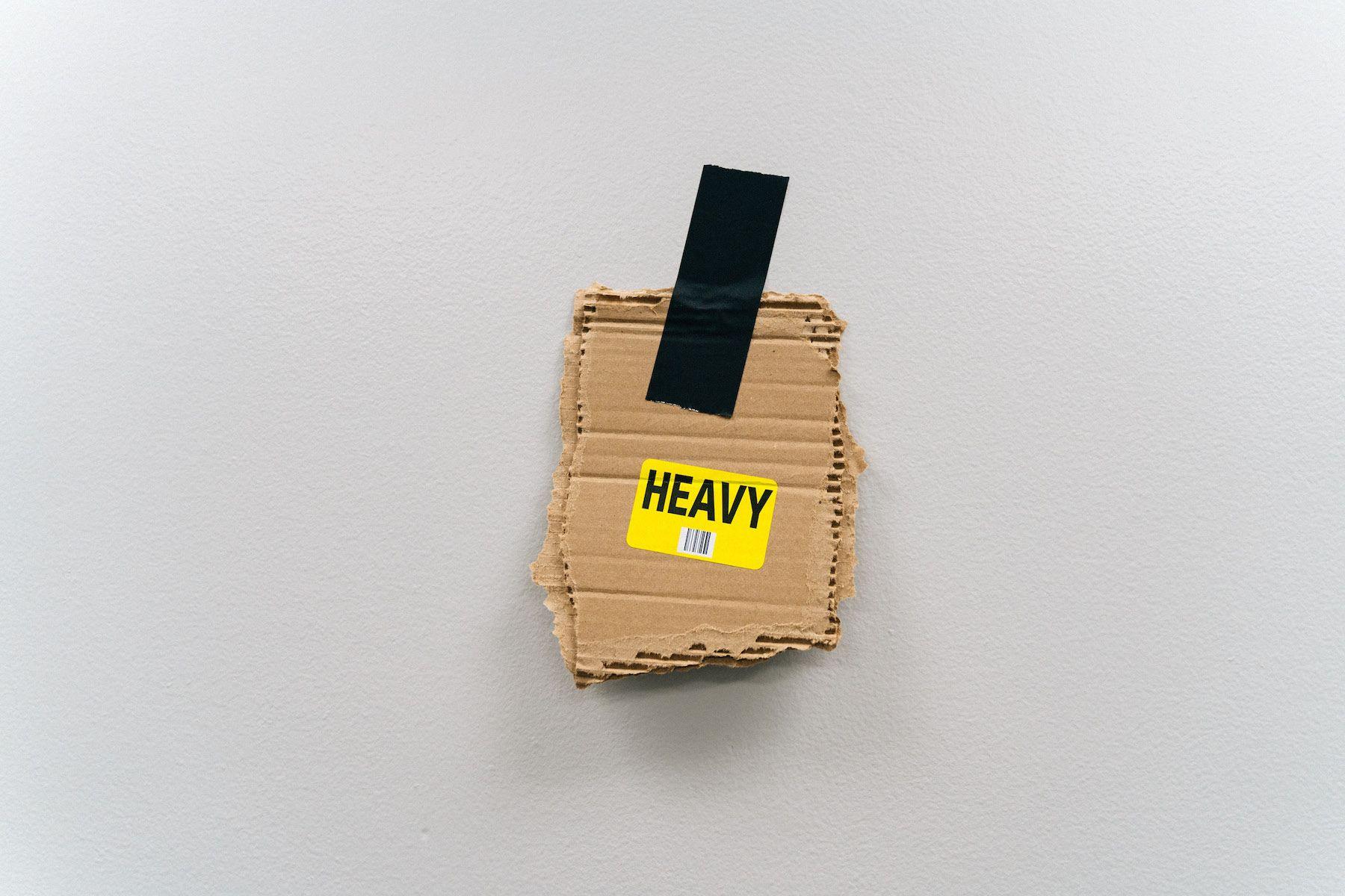 En flyttkartongbit uppklistrad på väggen med texten "heavy"