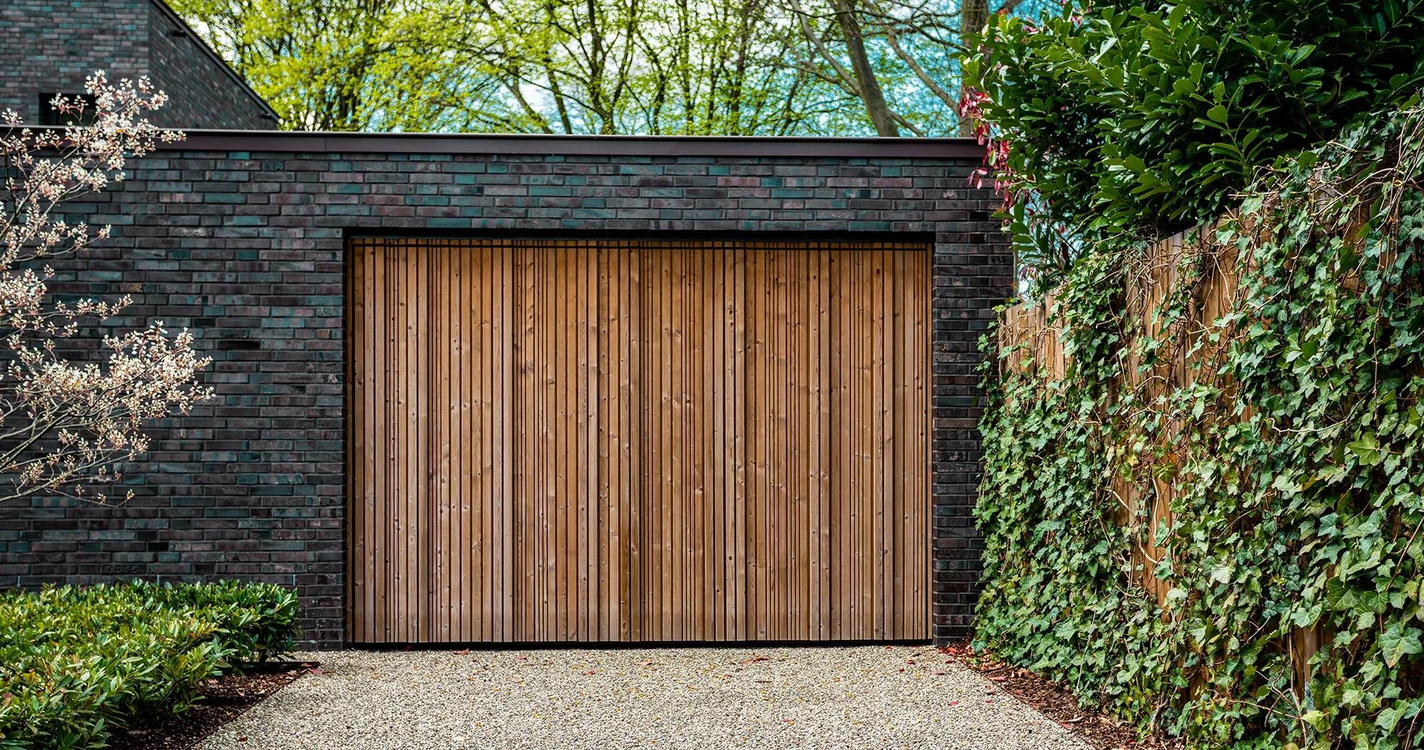 Tegelhus med elegant garagedörr och carport, omgiven av ett vackert staket klätt i murgröna - Skapa funktionella och stilfulla utrymmen med våra garage- och carporttjänster.