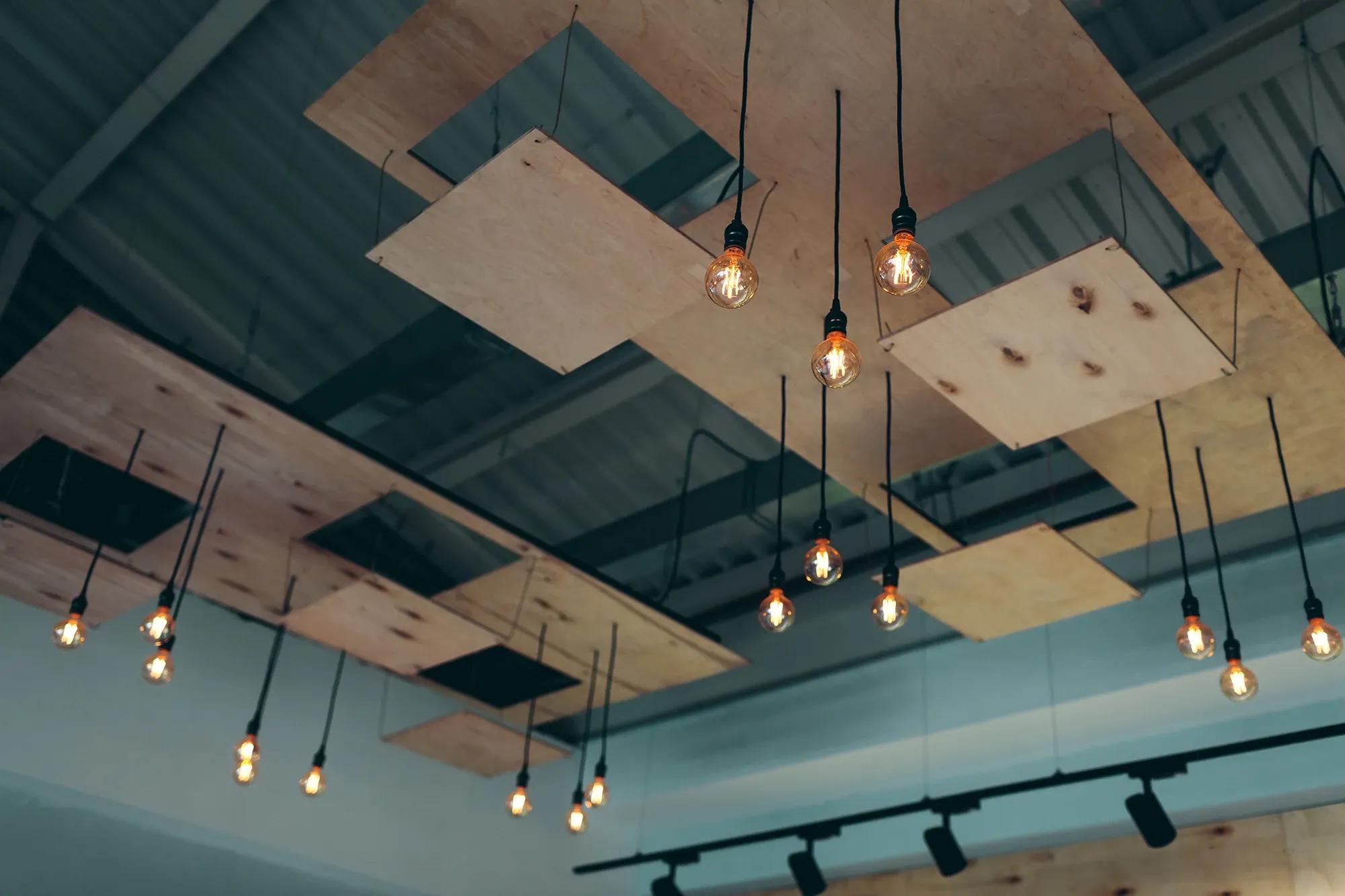 Modernt innertak i industrial och popkonststil med hängande glödlampor, utfört i kontorslokal av proffs och hantverkare inom undertak och akustik