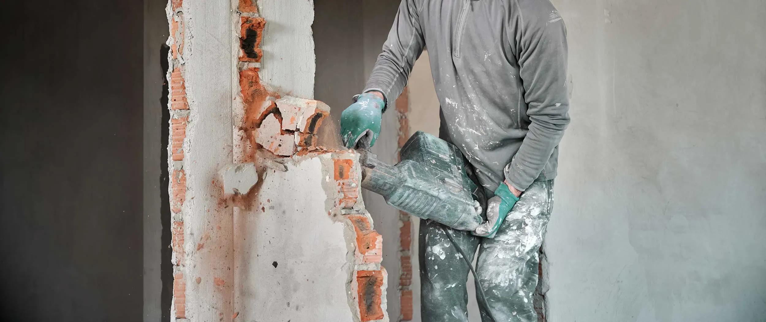 Arbetare i skyddshjälm med perforator som slutför dekonstruktion av tegelvägg