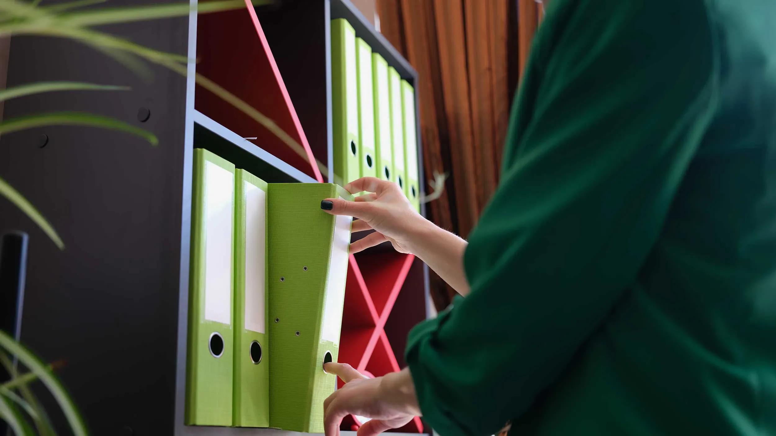Kvinna organiserar bokföringsdokument i en grön pärm och placerar den i hyllan