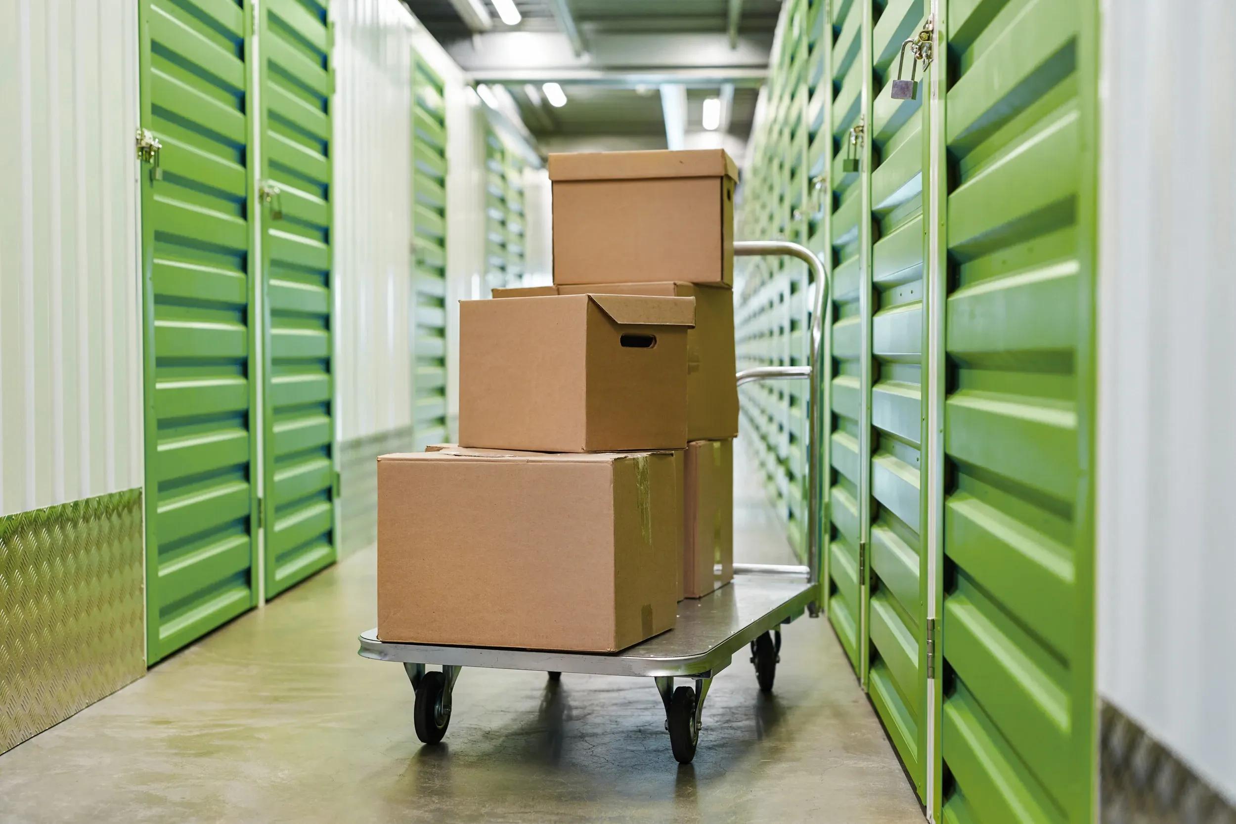 Magasinering av organiserade lådor på vagn i förrådslokal med gröna dörrar och lås - Flexibel och säker förvaring med våra magasinerings- och förrådstjänster.