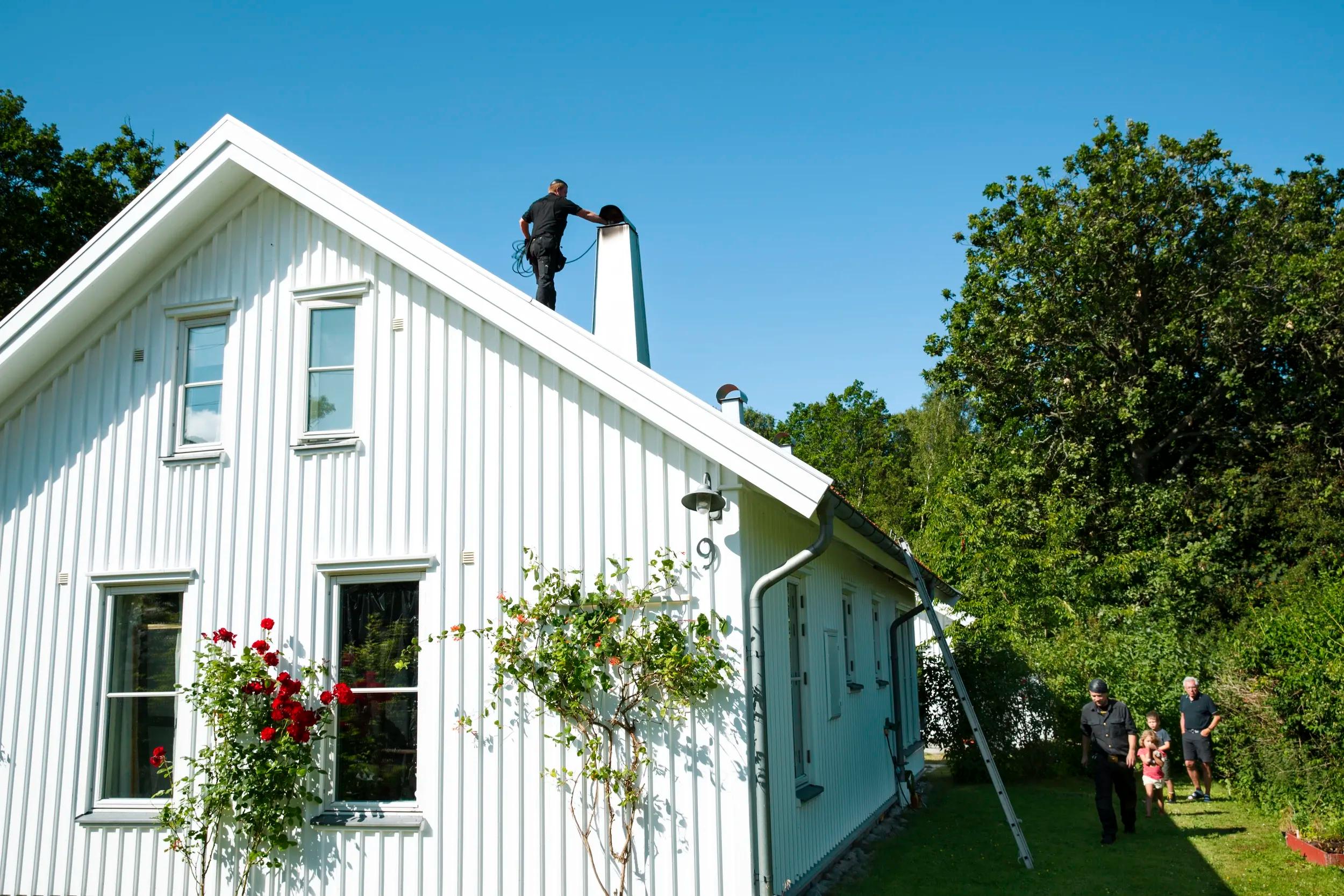 Erfaren sotare står på taket av ett vitt hus och arbetar