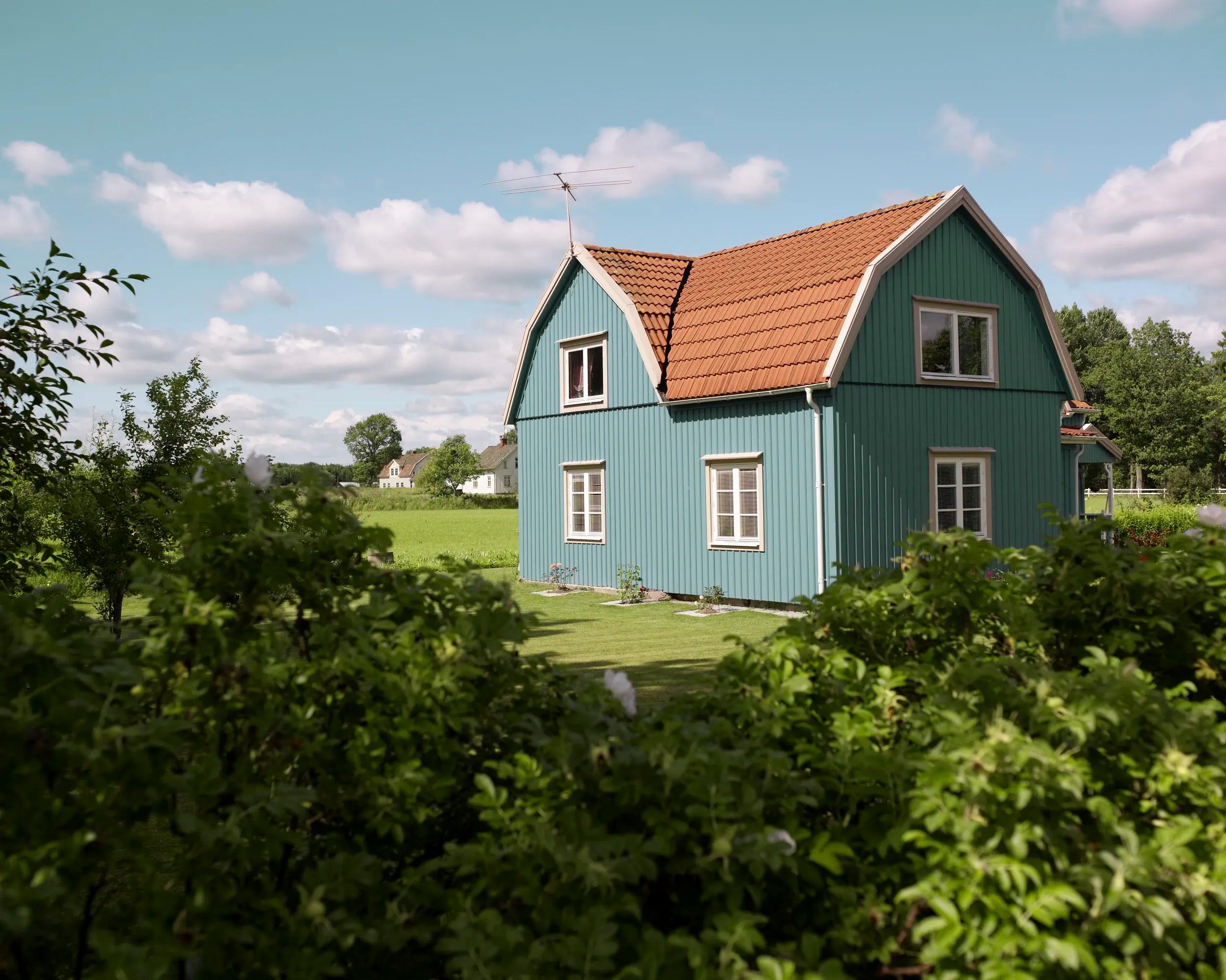 Idylliskt turkost hus omgivet av frodig trädgård och färgglada rabatter - symboliserar dräneringstjänst för effektiv och pålitlig hantering av vattenavledning och skydd av din bostadsgrund