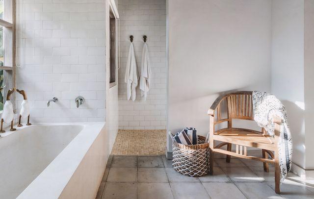 Ett stilrent och minimalistiskt badrum med betong och vitt kakel. Badrummet har ett badkar under fönstret och en trästol vid sidan.