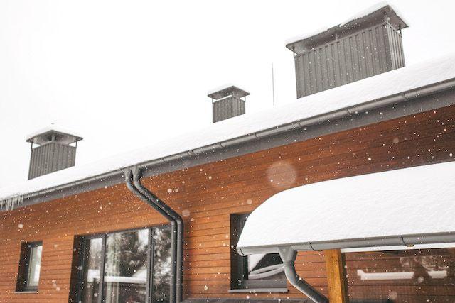 Hus med snö på taket, svarta stuprännor och träpanel