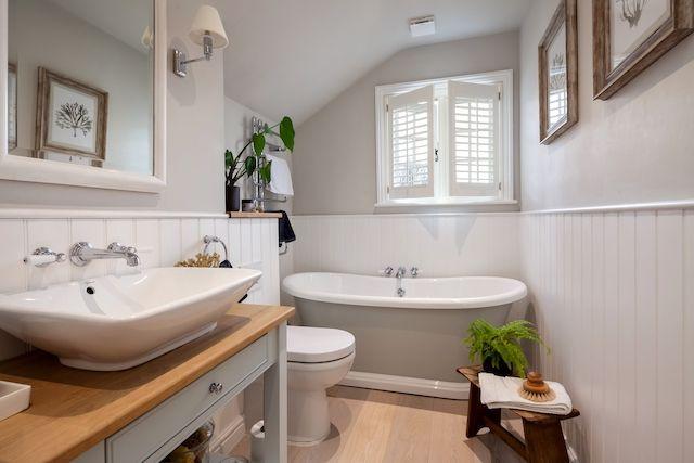 Ett fint renoverat badrum med grå kommod och grått badkar. Ett litet fönster står öppet ovanför badkaret.