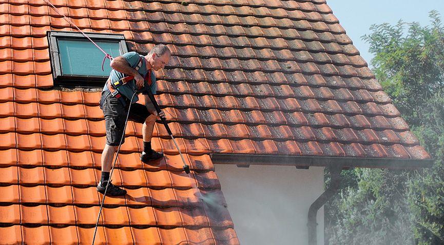 Man med säkerhetssele rengör tak med högtryckstvätt