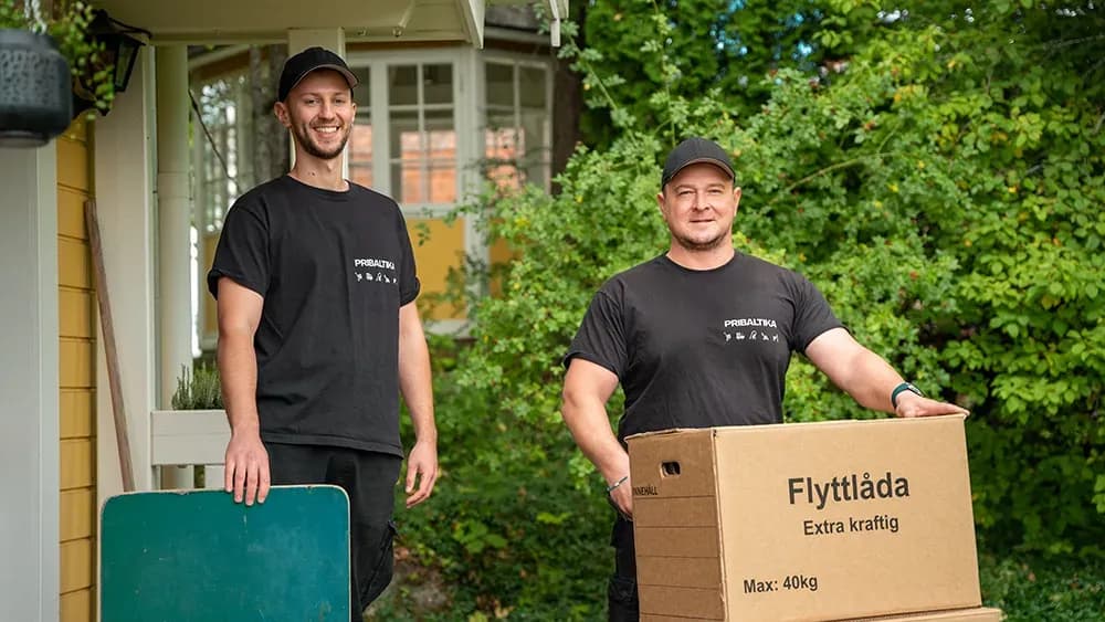 Flytthjälp med Pribaltika, flyttkillar håller i flyttkartonger och ler mot kamera