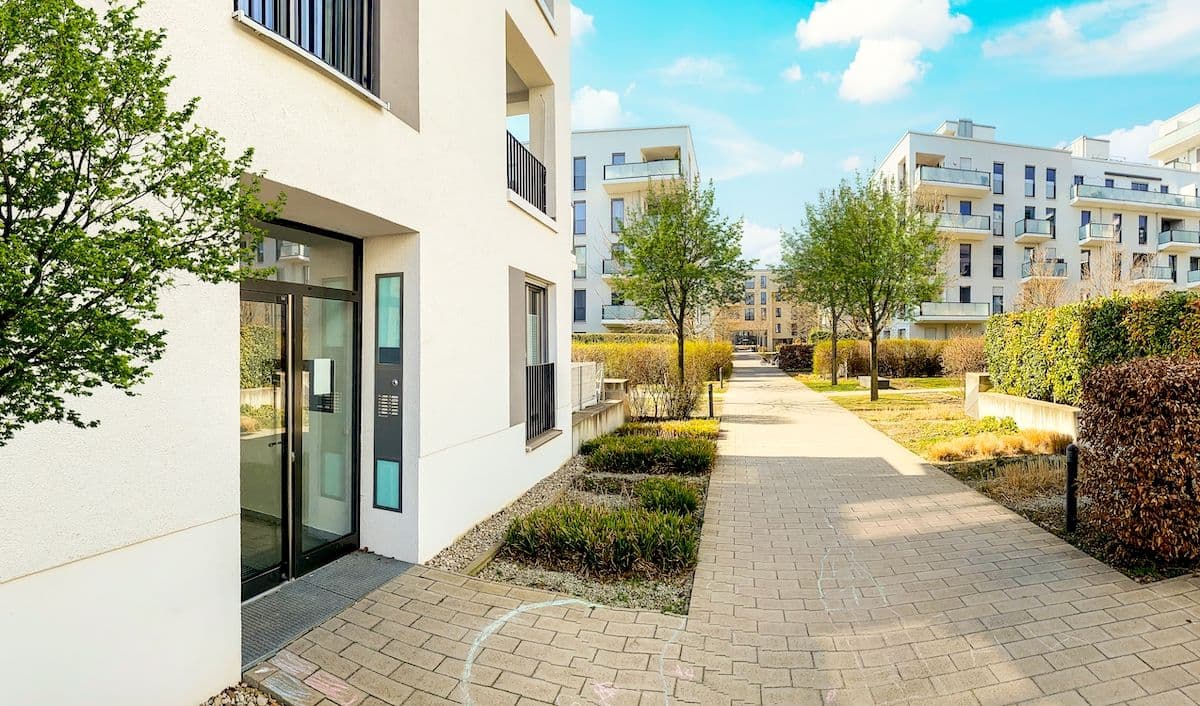 Bild på omgivningen vid ett lägenhetsområde med grönskande buskage och träd.