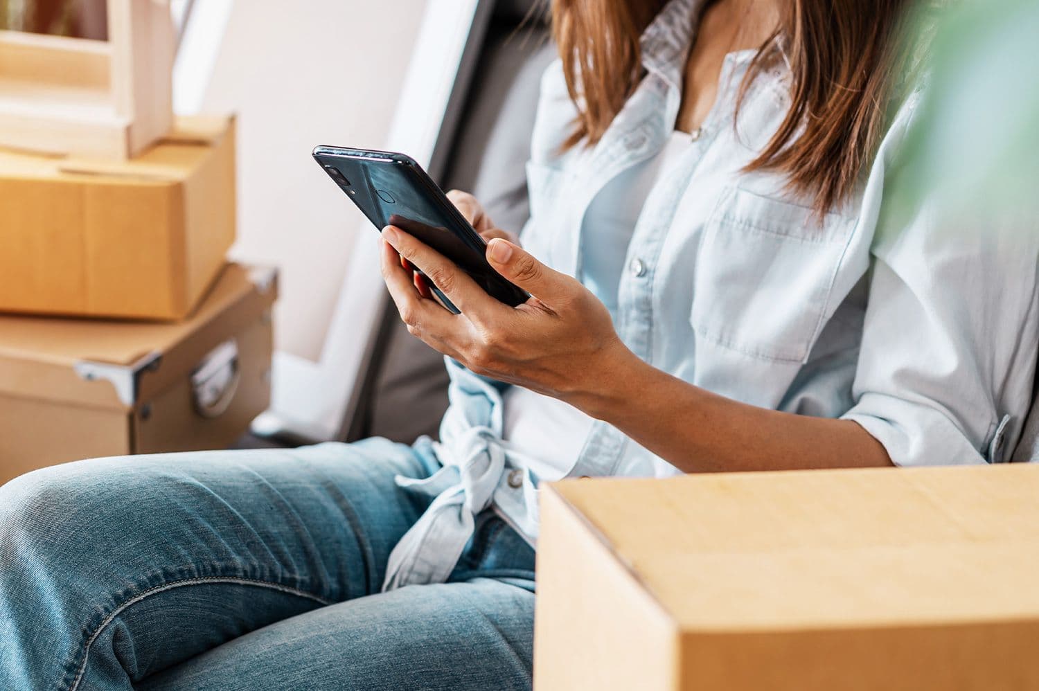 Kvinna som ska flytta sitter bredvid flyttkartonger och jämför flyttfirmor i app