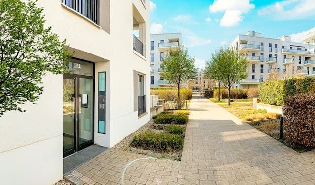 Bild på omgivningen vid ett lägenhetsområde med grönskande buskage och träd.