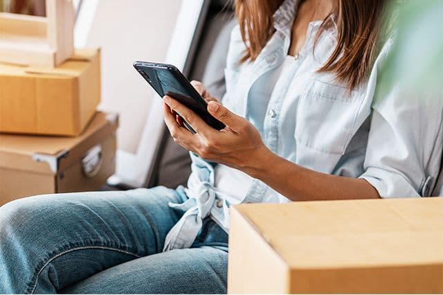 Kvinna som ska flytta sitter bredvid flyttkartonger och jämför flyttfirmor i app