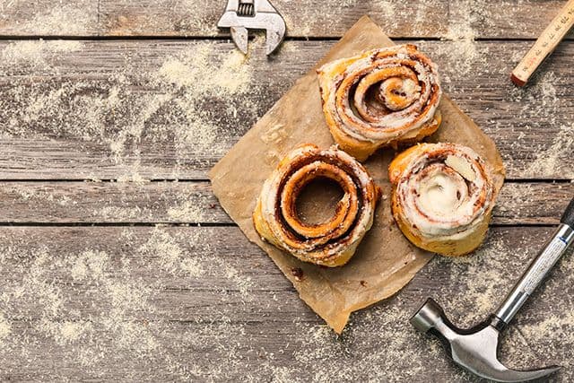 Fika för hantverkare med bullar, hammare och skiftnyckel ligger på ett arbetsbord i trä