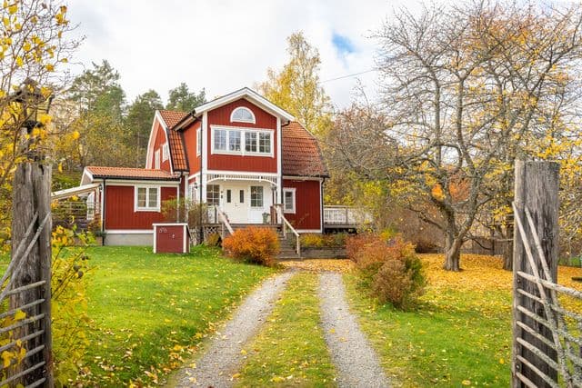 Rött hus med vita knutar i höstmiljö med gulnade löv på gräsmattan.