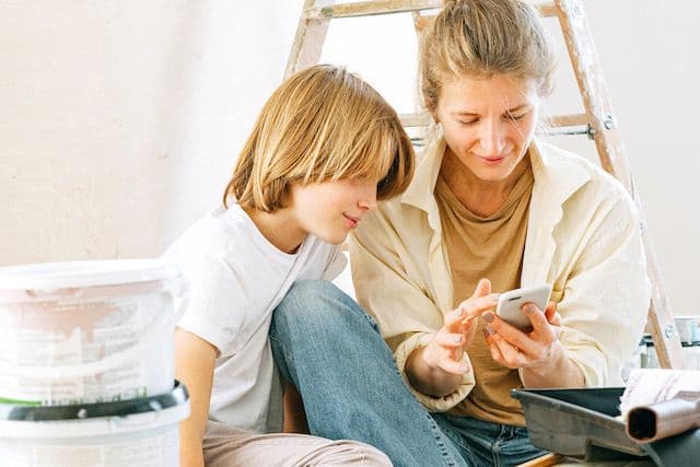 Mamma och barn kontrollerar företag innan de startar renoveringen.  Sitter bland färgburkar och en stege.
